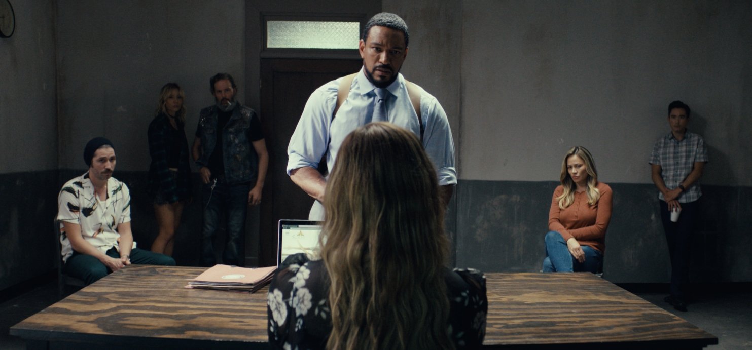 a group of people interrogate a blond woman sitting in a film still from detained